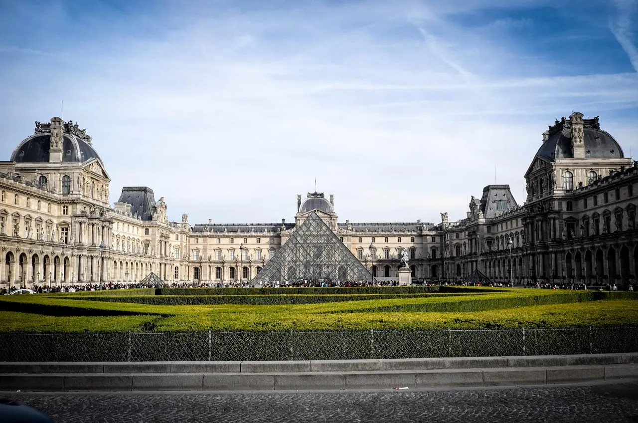 Die langen Flügel des Louvre rund um die Pyramide, über eine Rasenfläche hinweg gesehen