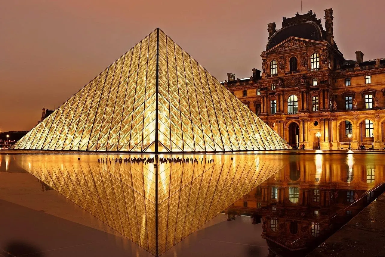 Die angestrahlte Louvre-Pyramide in der Abenddämmerung, gespiegelt in den Wasserbecken